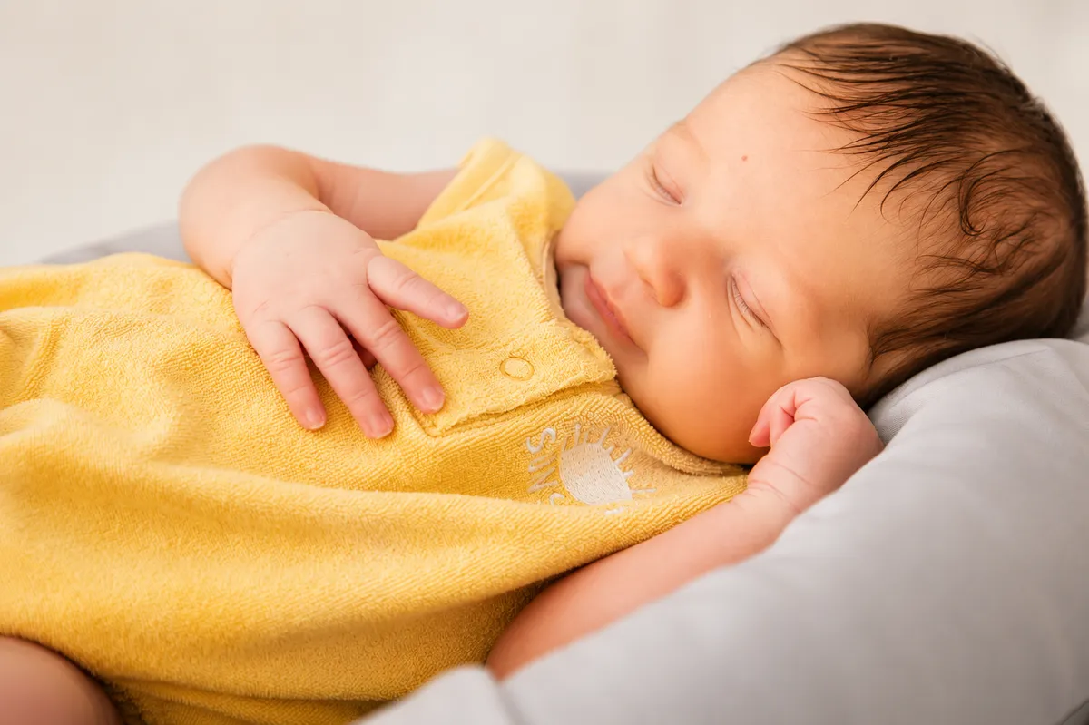Bébé endormi et heureux dans une barboteuse jaune soleil. Lumière douce et tamisée